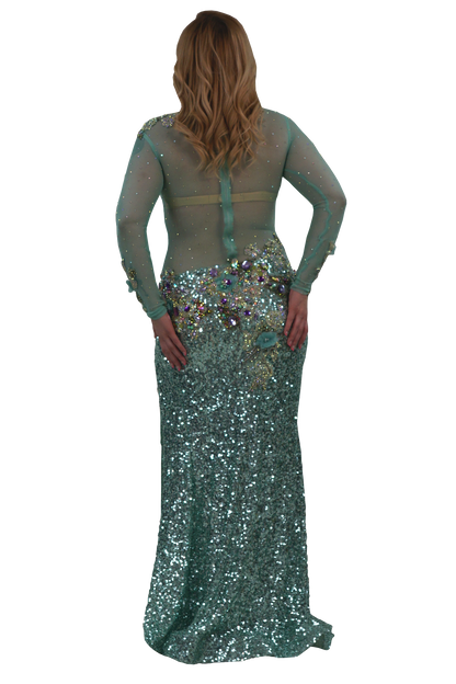 A woman modeling a floor-length teal sequined gown from the back, featuring sheer long sleeves, a structured back with a central strap, and a heavily embellished waistband with iridescent sequins and rhinestones, set against a plain white background.