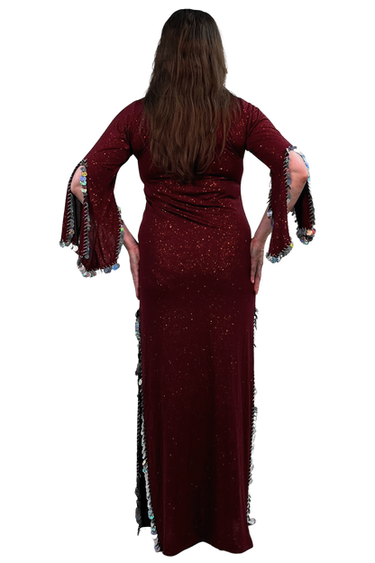 A woman viewed from the back wearing a long burgundy sequined maxi dress with fringed bell sleeves and side slits, set against a plain white background.