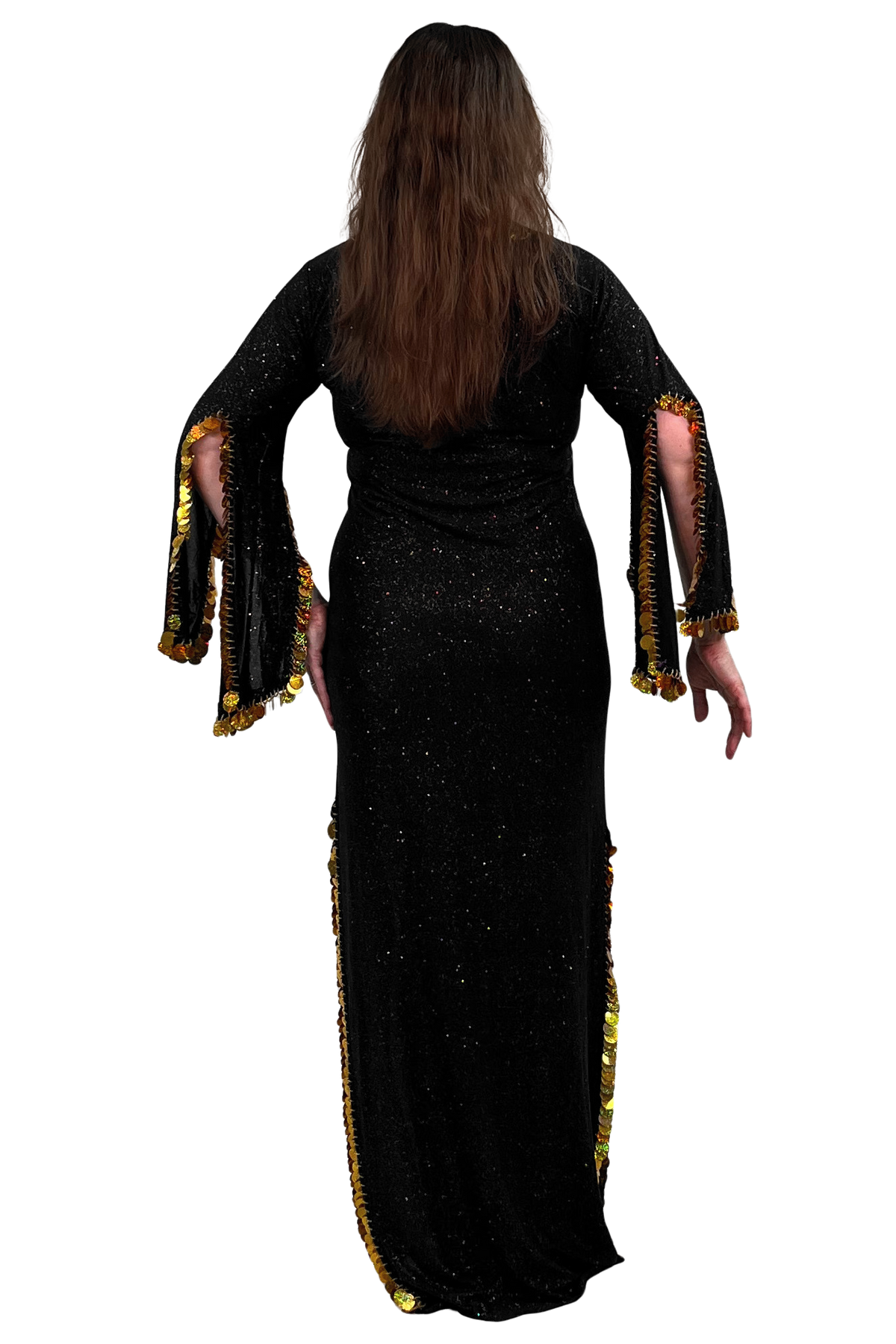 A woman viewed from the back wearing a long black glittery dress with wide flared sleeves and gold fringe trim along the sleeve edges and side slits, against a plain white background.