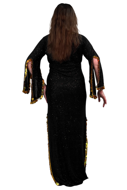 A woman viewed from the back wearing a long black glittery dress with wide flared sleeves and gold fringe trim along the sleeve edges and side slits, against a plain white background.