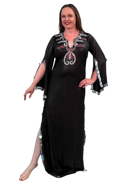 A woman modeling a brown maxi dress with silver and red sequin details on the neckline and silver sequined trim on the sleeves and side slit, set against a plain white background.