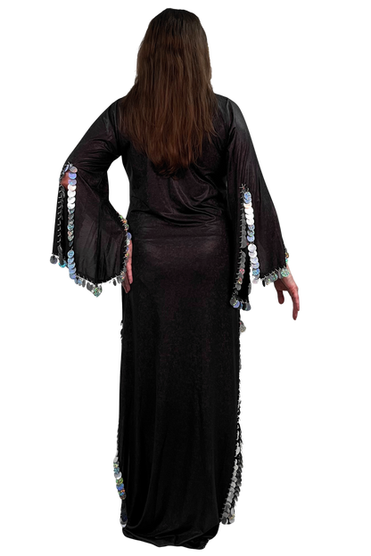 A woman viewed from the back wearing a long black dress with wide bell sleeves decorated with rows of silver paillette trim, standing against a plain white background.