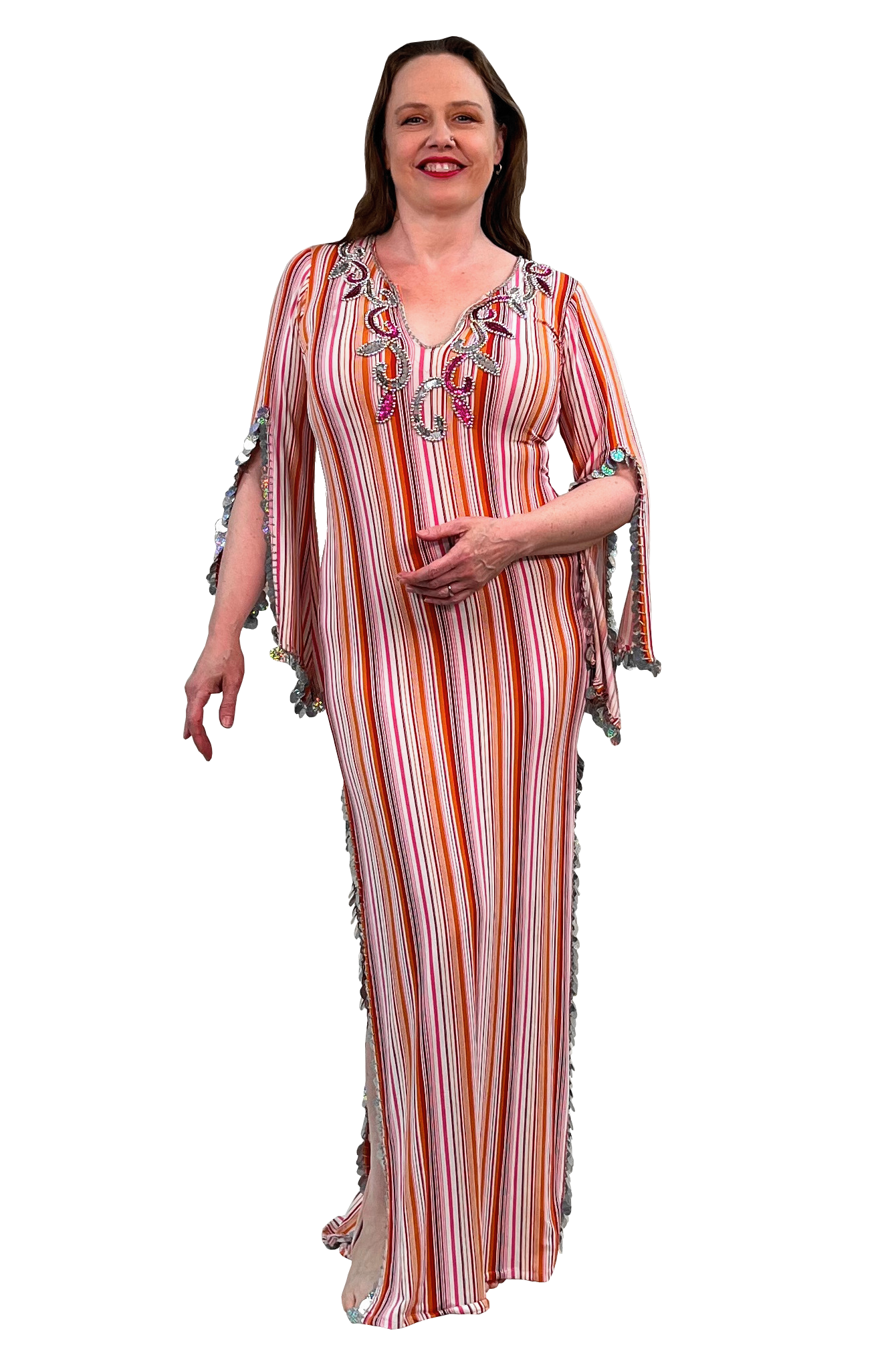 A woman modeling a long, sleeveless maxi dress with vertical orange, pink, white, and red stripes, featuring colorful embroidered details on the neckline and fringed trim on the sleeves and sides.