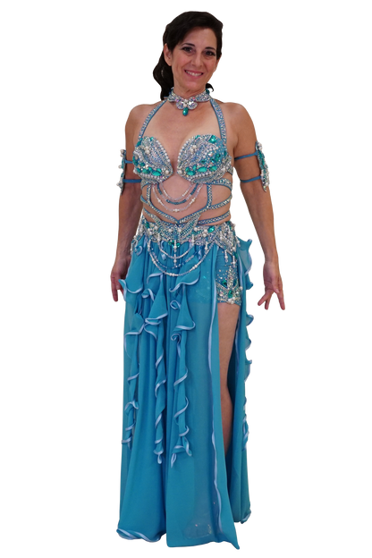 A woman modeling a turquoise and silver belly dance costume with a matching embellished bra top, hip scarf, arm bands, and a long ruffled skirt on a plain white background.