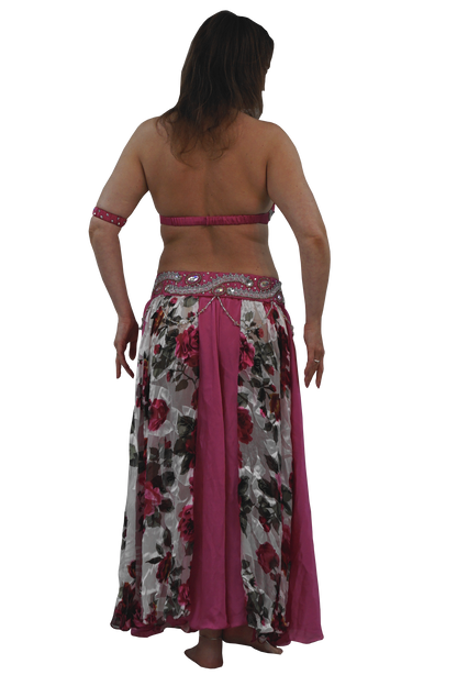 A woman shown from the back wearing a belly dancing costume consisting of a floral print skirt with a solid magenta lining and a matching magenta halter top with a matching armband, set against a plain white background.