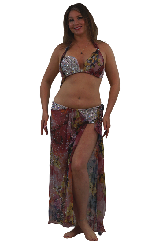 A woman modeling a two-piece belly dance set consisting of a silver sequined bra top and a matching long, sheer sarong skirt with a multicolor floral print.