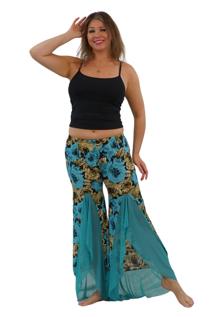 A woman modeling a pair of wide-leg bohemian-style pants with a teal, gold, and black floral print, paired with a black tank top, against a solid white background.