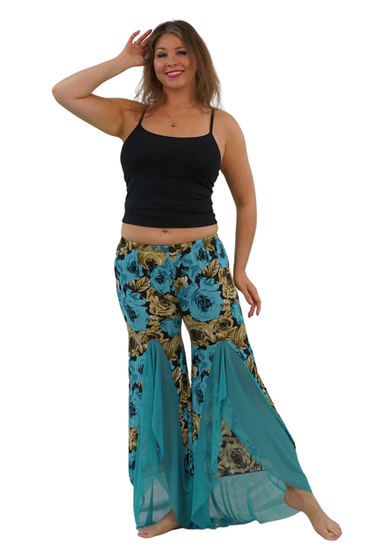A woman modeling a pair of wide-leg bohemian-style pants with a teal, gold, and black floral print, paired with a black tank top, against a solid white background.