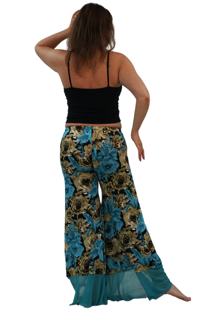 A woman shown from the back wearing wide-leg bohemian-style pants with a blue, gold, and black floral pattern, paired with a black camisole, against a plain white background.